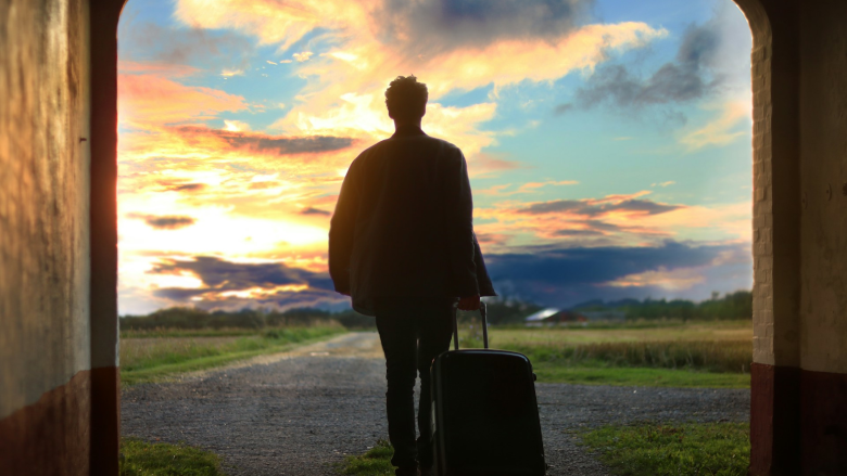 Man with suitcase walking toward sunrise